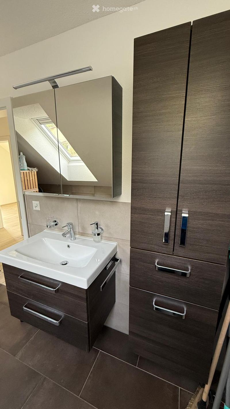 Modern bathroom with a white sink, dark wooden cabinets, a large mirror with built-in lighting, and a sleek faucet.