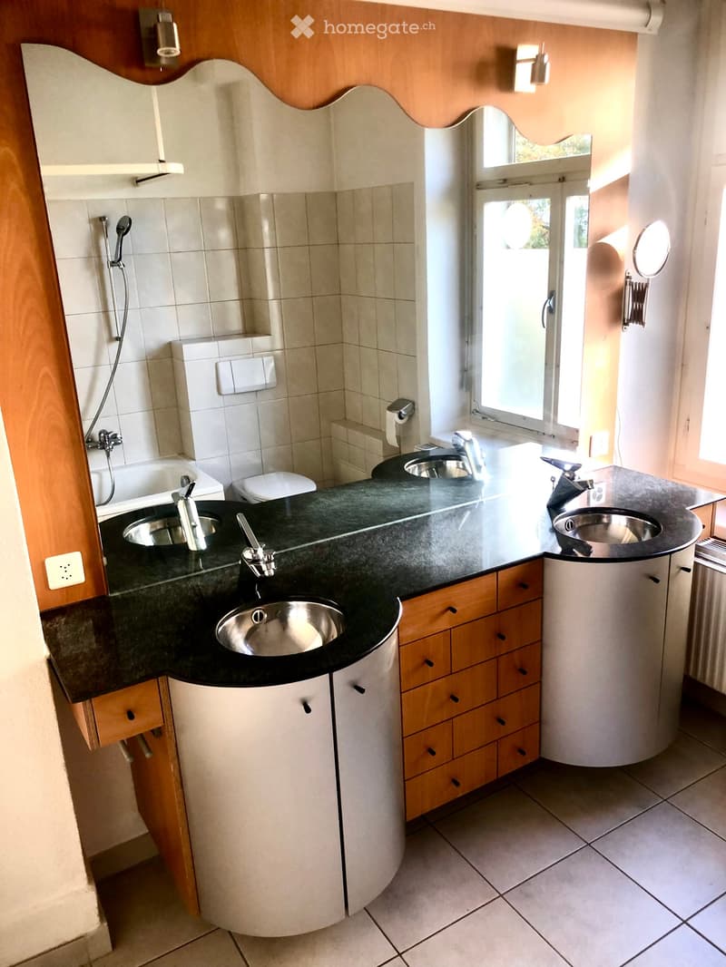 Modern bathroom with double sink vanity, mirrored cabinet, bathtub, and toilet. Features wooden cabinets and tiled walls.