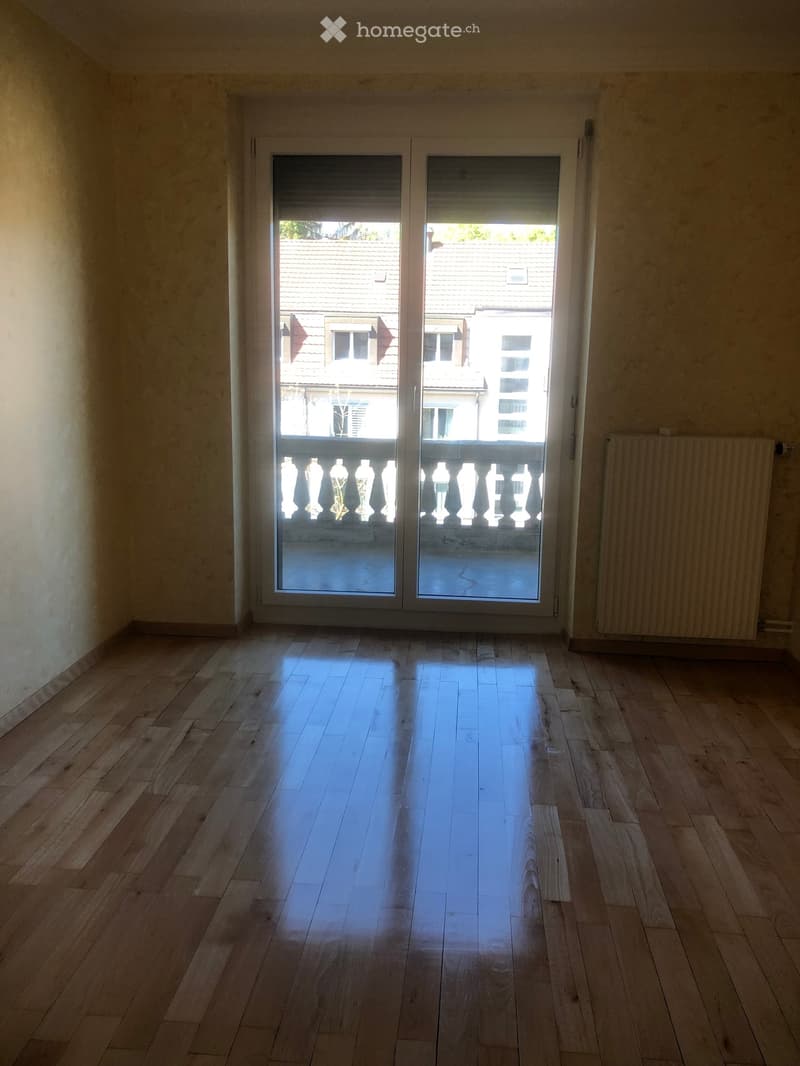 Empty room with wooden flooring, large sliding glass doors leading to a balcony, and a radiator on the right wall.