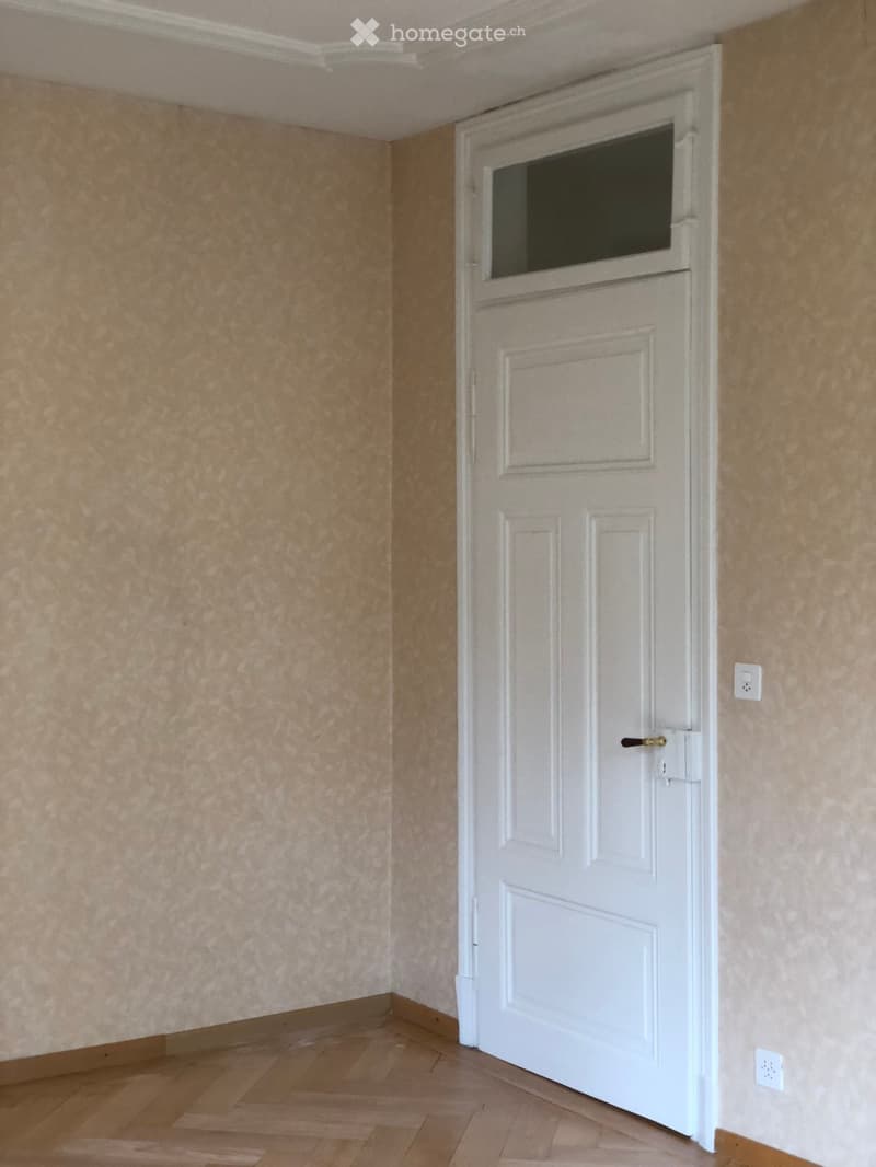 Empty room with wooden flooring, beige walls, and a white door with a window at the top.