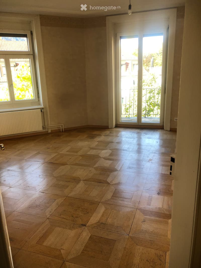 Empty room with wooden floor, large windows, and sliding glass doors leading to a balcony.