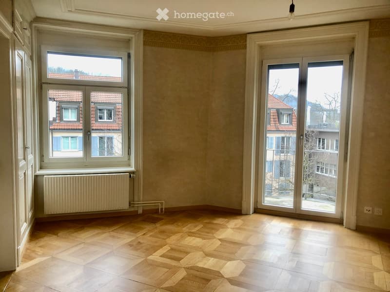 Empty room with wooden flooring, large windows, radiator, and sliding glass doors leading to a balcony.