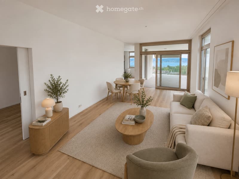 Modern living room with light wood flooring, white walls, and large windows. Features a cream-colored sofa, round coffee table, side table with lamp, dining area with chairs and table, and decorative plants.