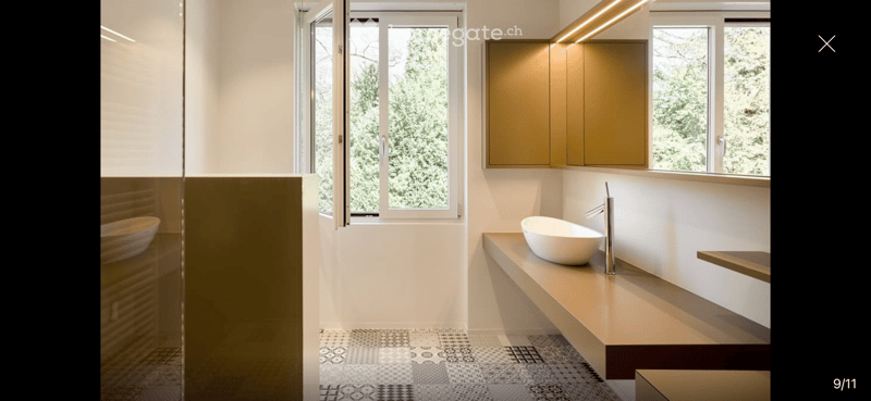Modern bathroom with a sleek sink, faucet, and built-in cabinet. Features a large window with a view of greenery, and a decorative bowl on the counter.