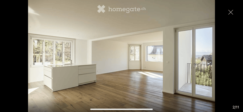 Bright, unfurnished room with wooden flooring, large windows, and a sliding glass door leading to a balcony with scenic views.