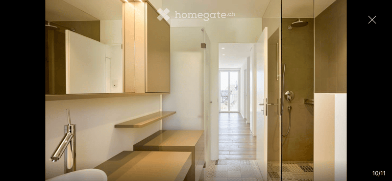 Modern bathroom with a sleek sink, mirror, and glass-enclosed shower area. The space features light-colored tiles and wooden flooring.