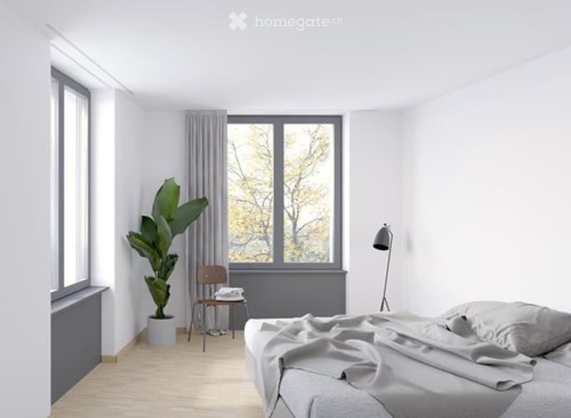 Modern, minimalist bedroom with a large window, grey bedding, a wooden chair, a small table, a floor lamp, and a potted plant.