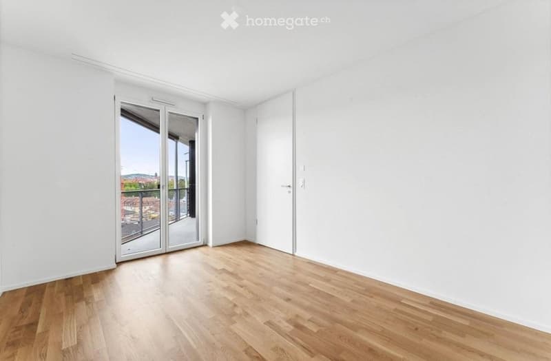 Empty room with white walls, wooden floor, and large sliding glass door leading to a balcony.