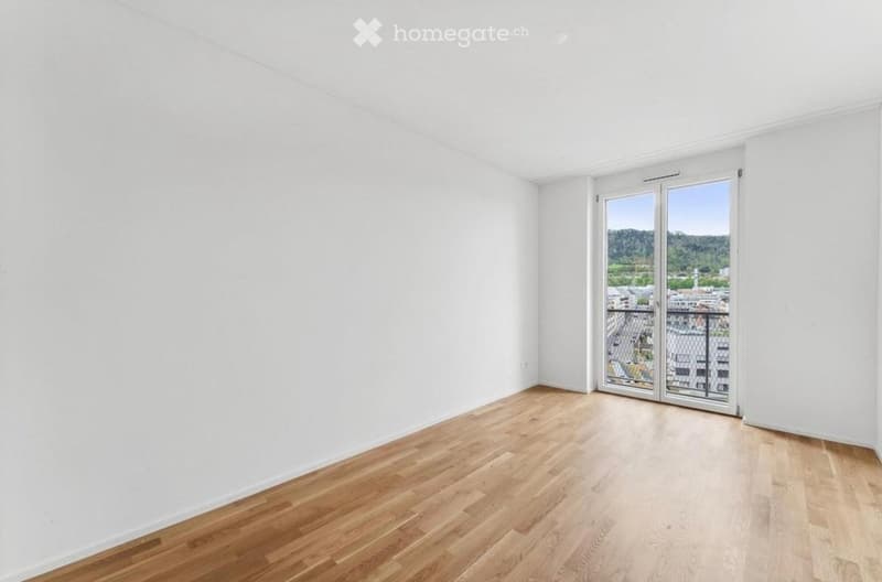 Empty room with white walls and wooden flooring, featuring a large sliding glass door leading to a balcony with a city view.