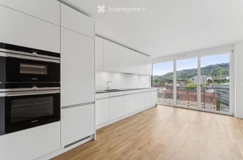 Modern kitchen with white cabinets, stainless steel oven, and large windows offering a scenic view.