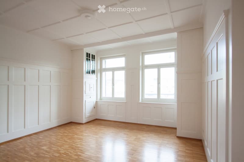 Empty room with white walls, wooden floor, and large windows allowing natural light. No furniture or equipment present.