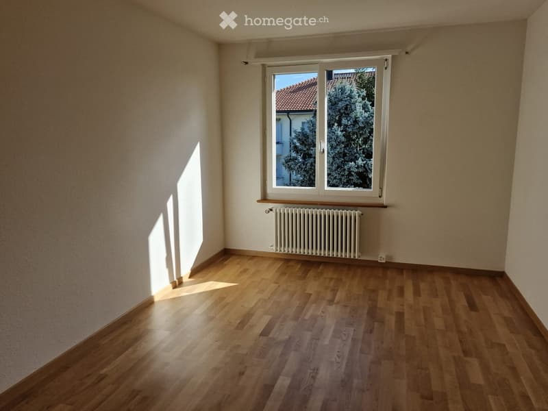 Empty room with wooden flooring, white walls, and a window with a radiator below it.