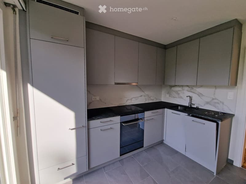 Modern kitchen with grey cabinets, black countertops, and a built-in oven. Features a marble backsplash and tiled flooring.