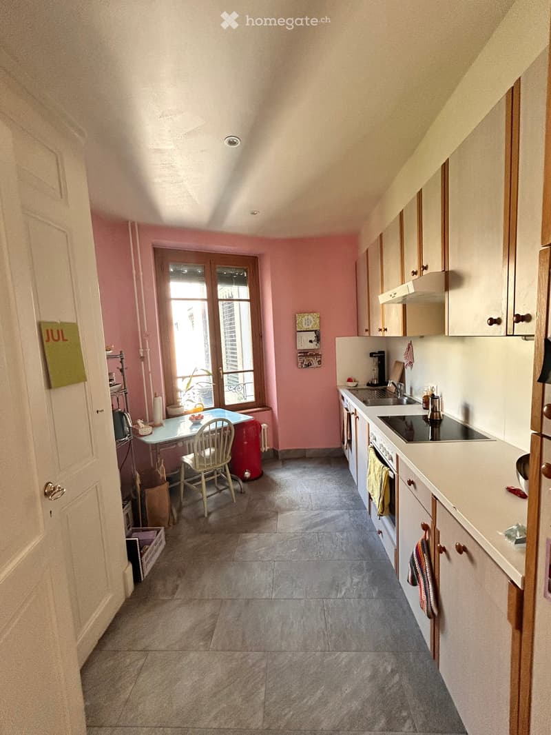 Bright kitchen with white cabinets, a central island, and a dining area with a table and chair. The space features a tiled floor and a large window with a view of the outside.