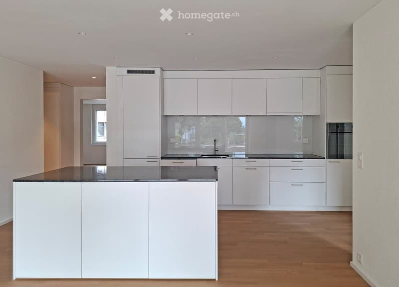 Modern kitchen with white cabinets, a central island, and a dark countertop. The space features a sleek design with a sink and faucet, and a window providing natural light.