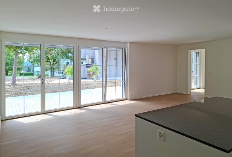 Empty room with wooden flooring, large sliding glass doors leading to an outdoor area, and a small black countertop in the corner.