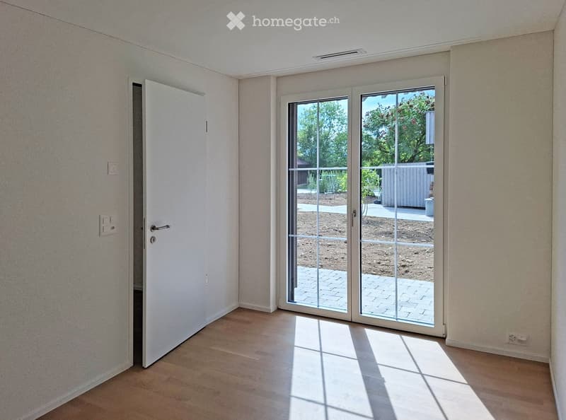 Empty room with light-colored walls, wooden flooring, and large sliding glass doors leading to an outdoor area.