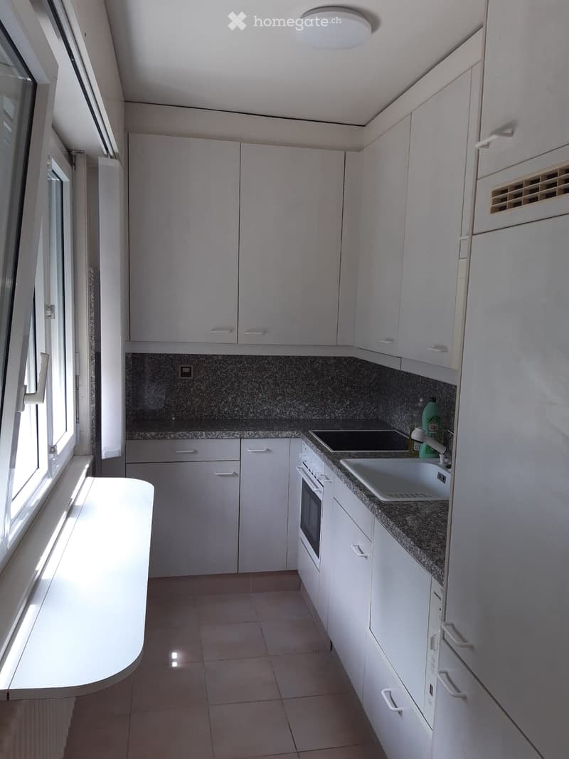 Modern kitchen with white cabinets, granite countertop, sink, stove, and oven. Features a large window allowing natural light to enter.