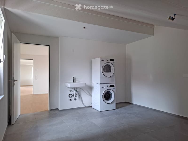 Modern, minimalist laundry room with a stacked washing machine and dryer, a small sink, and tiled flooring.
