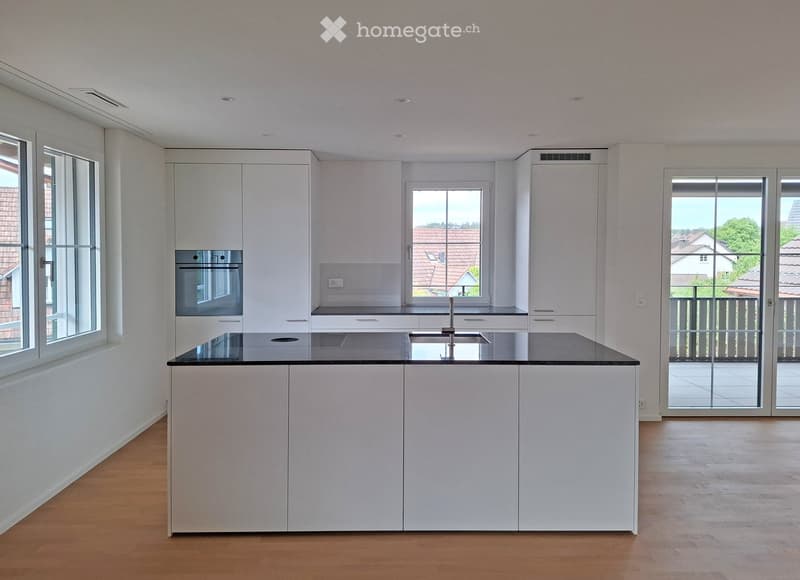 Modern kitchen with white cabinets, black countertop, central island, and large windows overlooking a residential area.