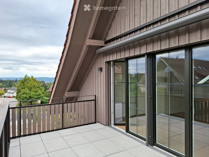 Balcony with tiled floor, glass sliding doors, wooden railing, and view of greenery and distant hills.