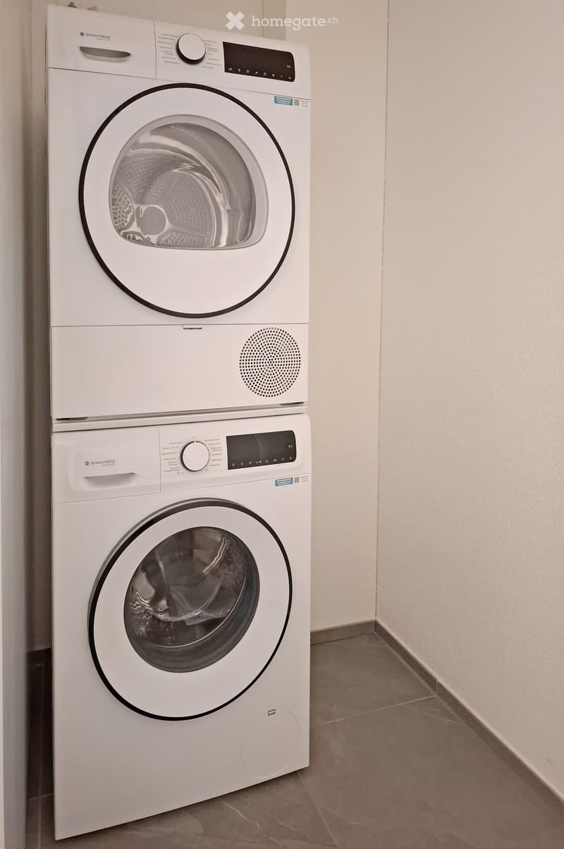 A compact bathroom with a stacked washing machine and dryer unit, featuring a sleek white design and modern control panels.