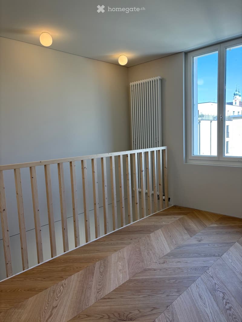 Empty hallway with wooden flooring, white walls, a radiator, and a window overlooking a cityscape.