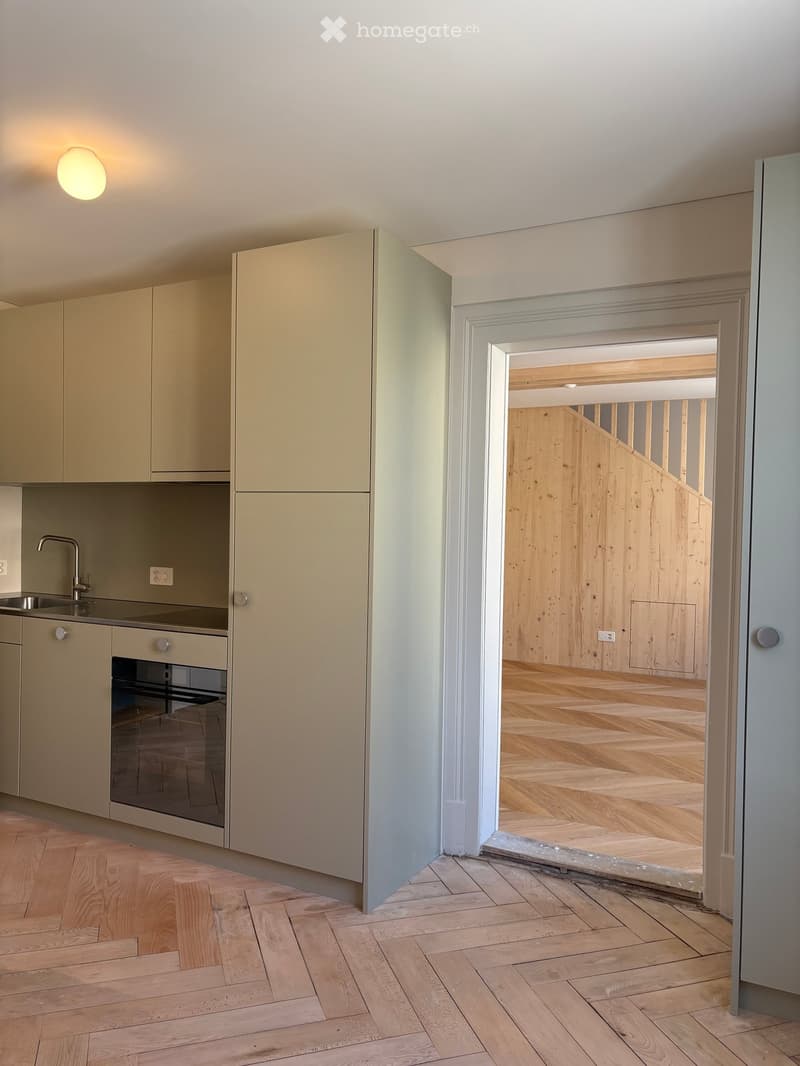 Modern kitchen with light-colored cabinets, a sink, and an oven, connected to a wooden staircase area.