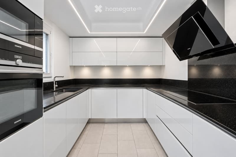 Modern kitchen with white cabinets, black countertops, built-in oven, range hood, and sleek faucet.