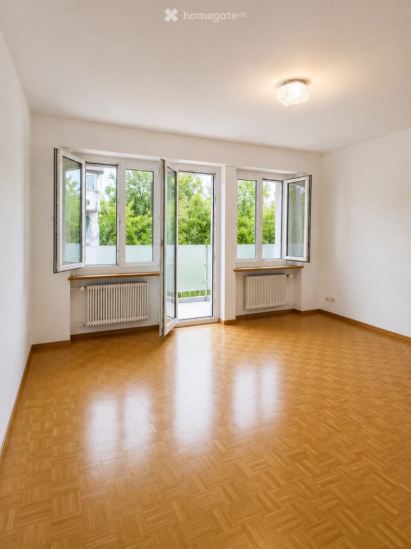 Empty room with wooden flooring, large windows, radiators, and a ceiling light fixture.