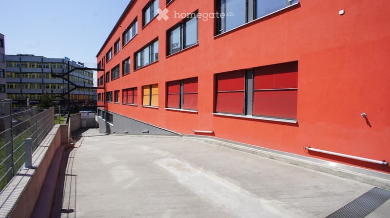 Red building with multiple windows, concrete pathway, metal railings, gray base