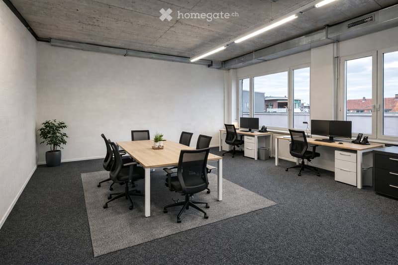 Modern office space with large windows, grey carpet, white brick walls, and industrial-style lighting. Includes a central meeting table with chairs, individual desks with computers, and potted plants.