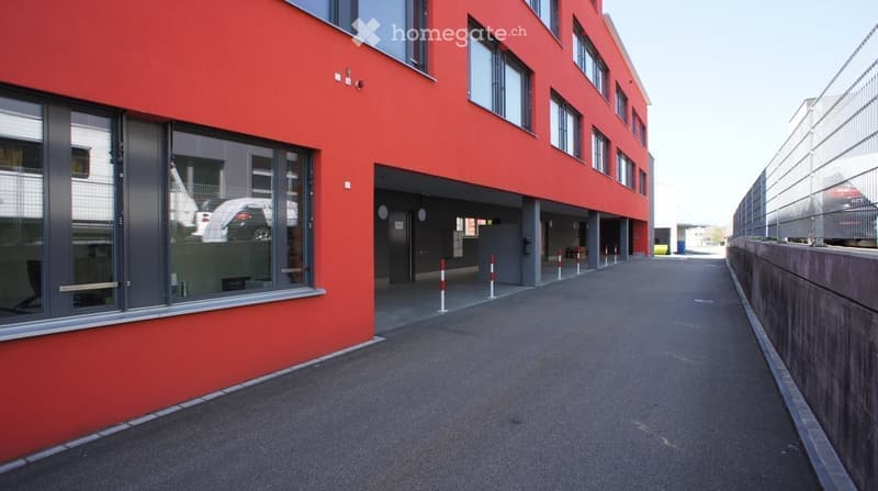 Red building with glass windows, parking lot, metal fence, empty