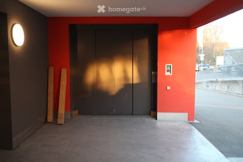 Empty garage with red walls, grey floor, and a large door.