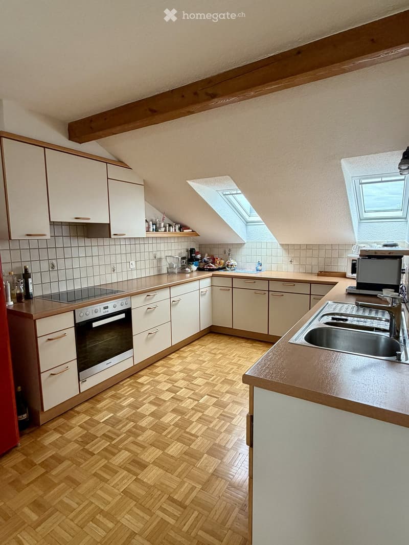 Modern kitchen with wooden herringbone flooring, white cabinets, stainless steel sink, oven, microwave, coffee maker, and various small appliances on the counter.
