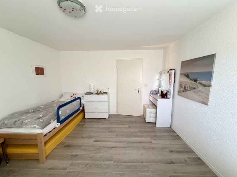 A small, modern bedroom with a single bed, nightstand, vanity mirror, and a large picture on the wall.