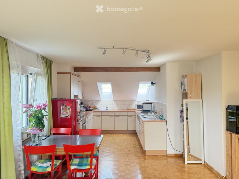 Bright kitchen with white cabinets, red refrigerator, wooden floor, and a dining area with red chairs and a table.