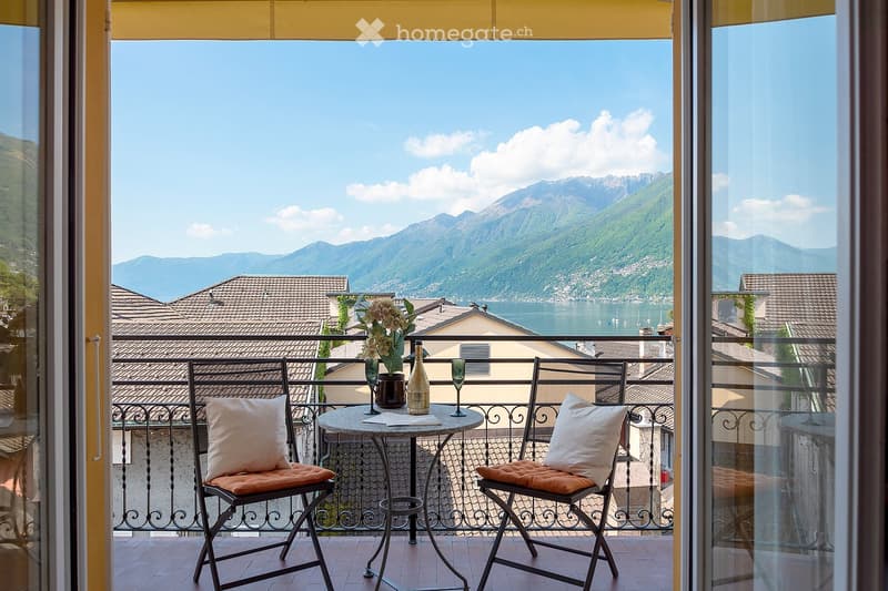 Balcony with a stunning view of the mountains and lake, furnished with a small table and two chairs, decorated with flowers and wine bottles