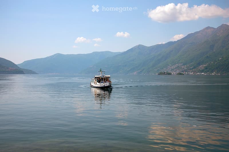 A scenic view of a lake surrounded by mountains, with a small ferry boat sailing across the calm waters.