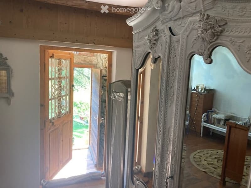 {"visible_features": ["Garden / Outdoor Area"], "type": "Furnished Room", "objects": ["wardrobe", "bench", "mirror", "table"], "description": "Elegant hallway with wooden floors, ornate antique wardrobe, open door leading to garden, small bench, and mirro