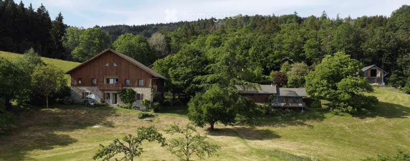 A scenic view of a rural property with multiple wooden houses surrounded by lush green trees and rolling hills.