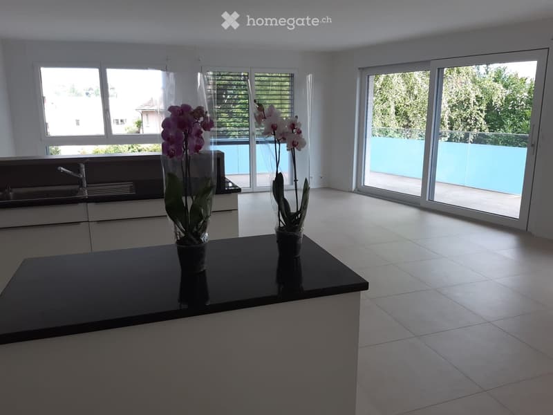 Modern kitchen with white cabinets, black countertop, and large windows leading to a balcony. Two vases with orchids are placed on the island.