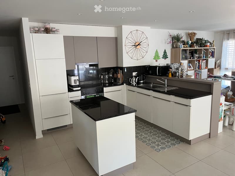 Modern kitchen with white cabinets, black countertops, stainless steel appliances, and a central island. Features a sink, microwave, coffee maker, and decorative items on shelves and countertops.
