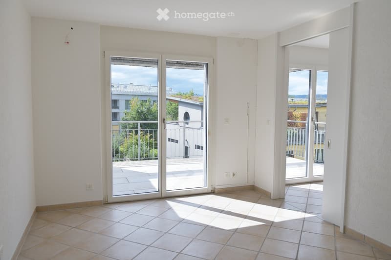Empty room with tiled flooring, white walls, and large sliding glass doors leading to a balcony with a view of the surrounding area.