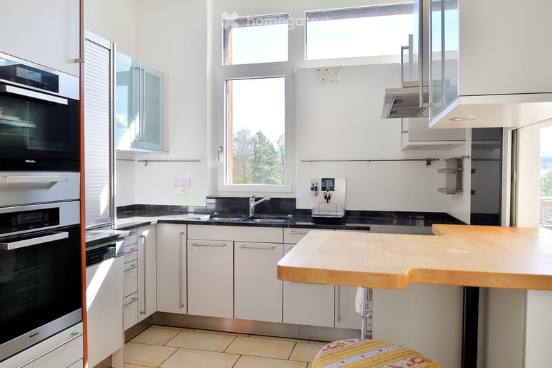 Modern kitchen with white cabinets, stainless steel appliances, a wooden island, and a small stool near the island.