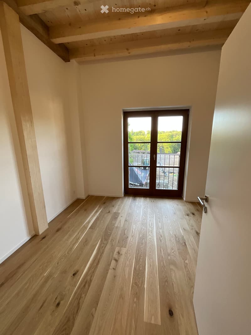 Empty hallway with light wooden flooring and white walls, featuring a glass door leading to a balcony area.