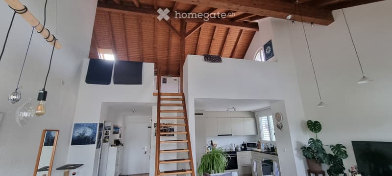 Open-plan living and kitchen area with exposed wooden beams, white walls, pendant lights, and modern kitchen appliances.