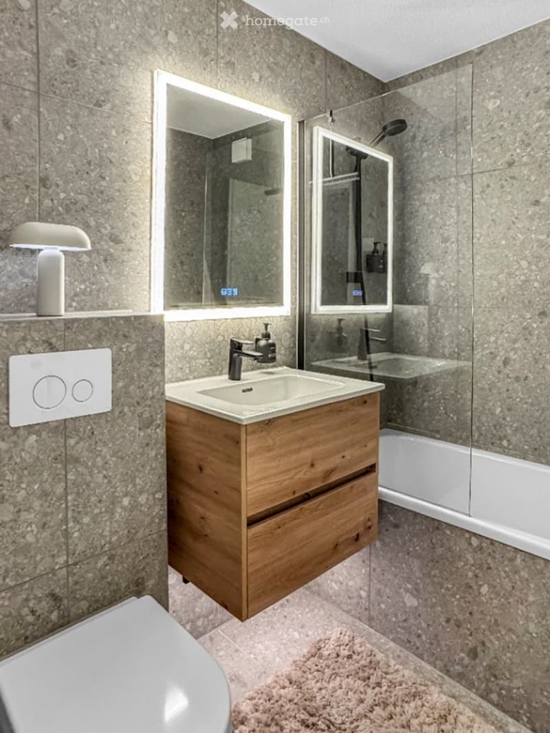 modern bathroom with gray tiles, white sink, wooden cabinet, glass shower, toilet, and mirror