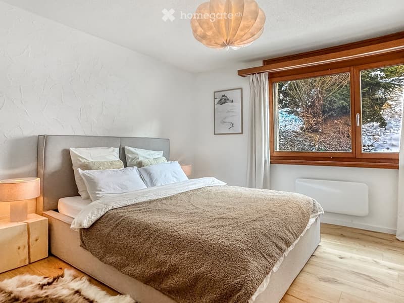 Wooden floor, large bed, two nightstands with lamps, cozy winter scene through window