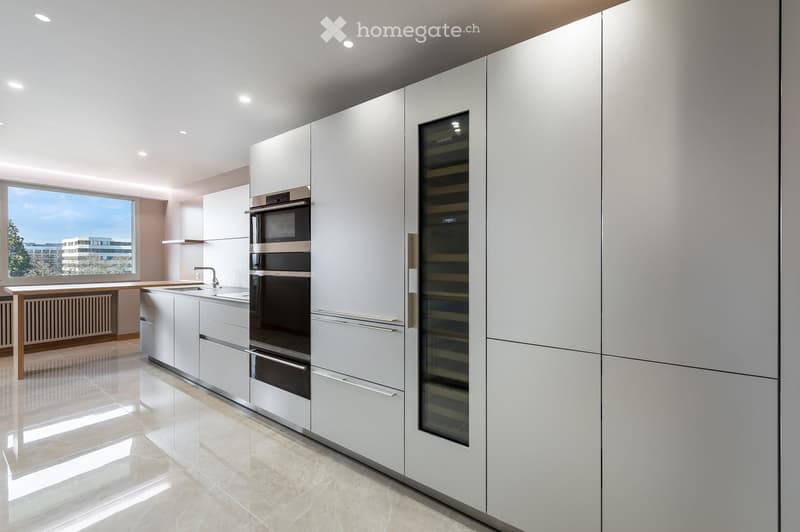 Modern kitchen with white cabinets, stainless steel appliances, a wine cooler, and a large window offering a view of the city.